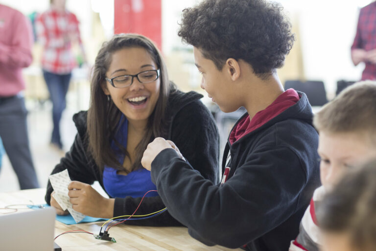 teens laugh while working on wiring a robotics project