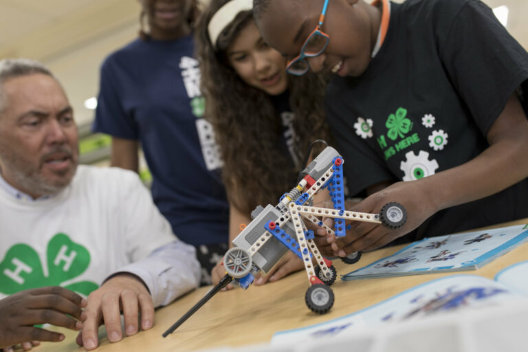 students work on a LEGO robot while adult observes