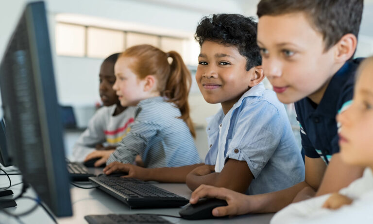 children work on computers as one child smiles at camera