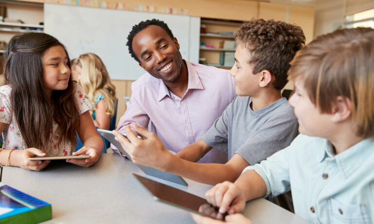 adult facilitator smiles as child shares projects on a tablet device